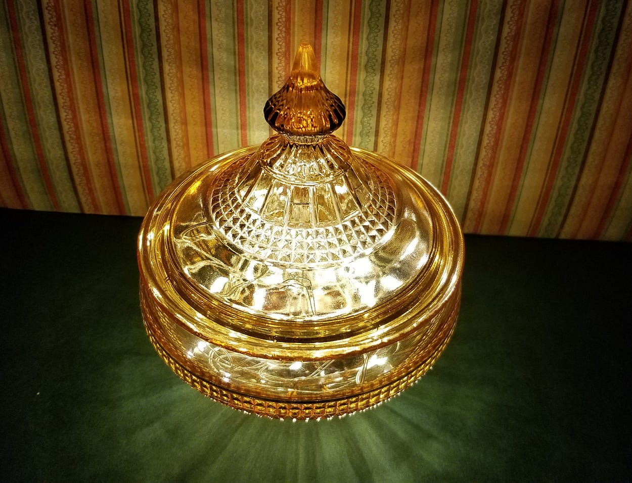 Fancy amber glass covered jar filled with miniature lights sitting on table illuminating an earth toned striped background.